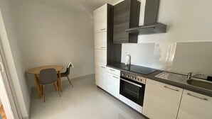 A modern kitchen with white cabinets, a black stove, and a small dining table with chairs.