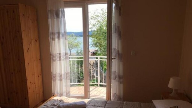 A bedroom with a bed, a wooden wardrobe, and a balcony with a view of trees and a body of water. - Apartments Roko- One bedroom apartment with balcony and sea view (B3) (Sveti Filip i Jakov)