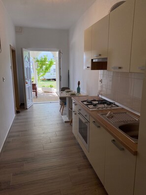 A modern kitchen with a central island, a stove, and a sink. A dining area is visible through an open door.