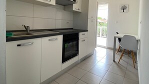 Eine moderne Küche mit weißen Schränken, einer schwarzen Arbeitsplatte und einem eingebauten Ofen. Durch eine offene Tür ist ein Essbereich mit Tisch und Stühlen zu sehen.