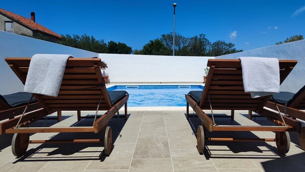 Area piscina con due lettini di legno, ciascuno con un asciugamano, e vista diretta sulla piscina.