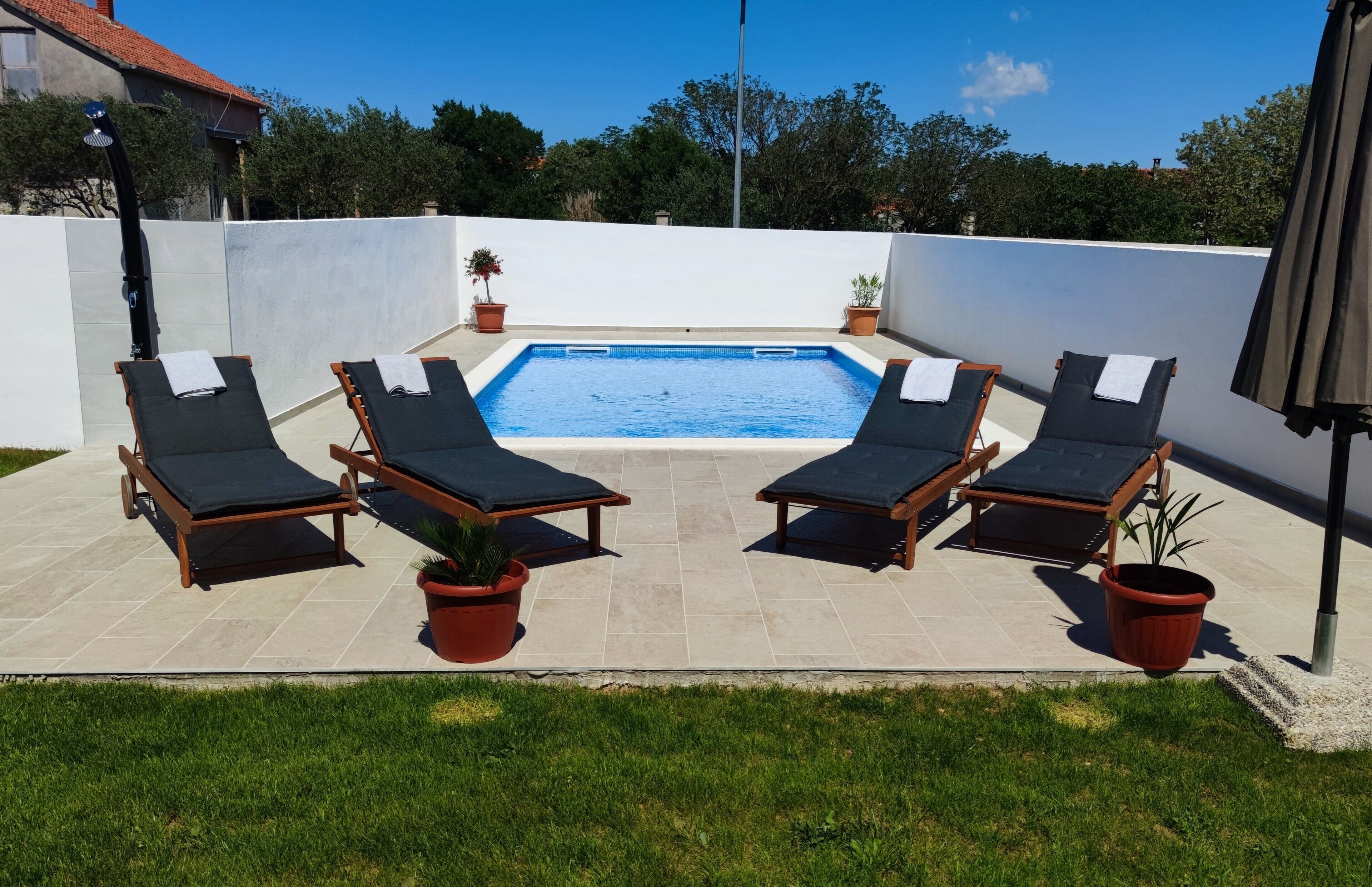 Une piscine entourée de quatre chaises longues et agrémentée de plantes en pot, le tout bordé d’un mur blanc et surplombé par un ciel d’un bleu limpide.