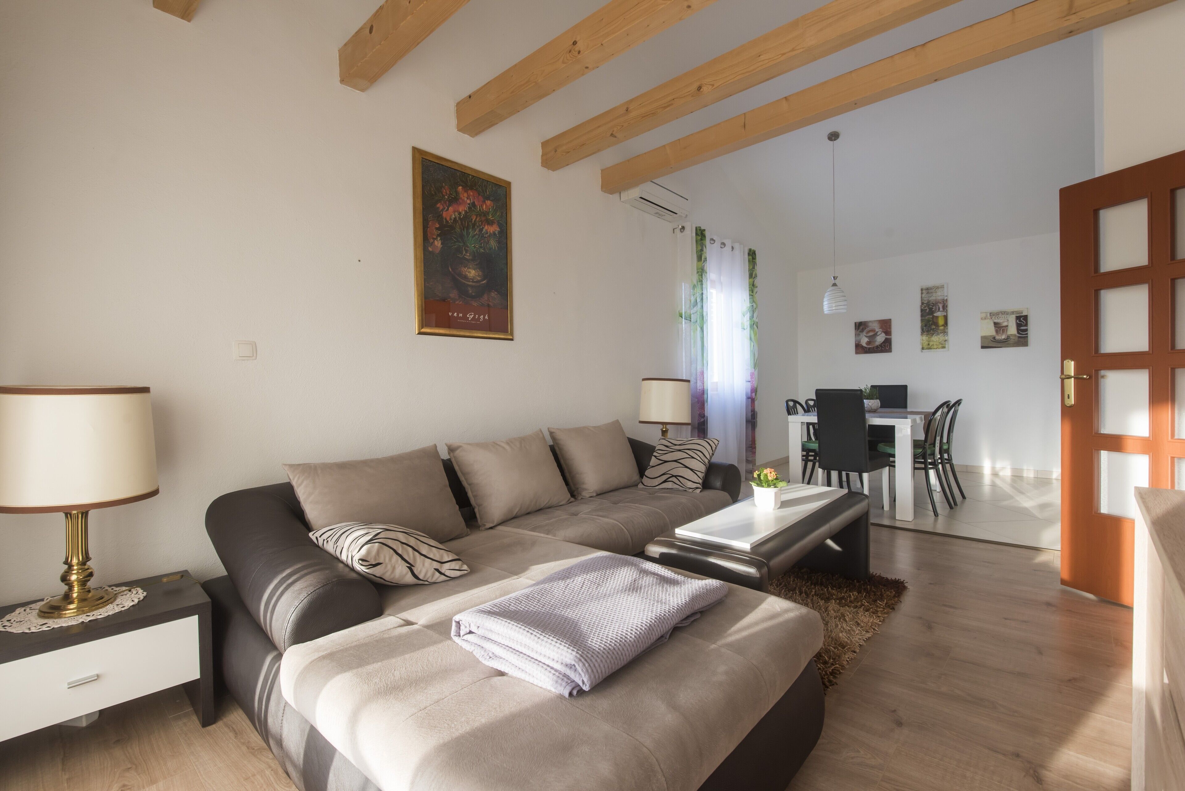 A modern living room with a sofa, a coffee table, and a lamp. There is a dining area with a table and chairs in the background.