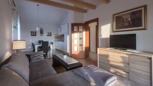 Un soggiorno moderno con divano, tavolino e TV. Sullo sfondo, una cucina con mobili e zona pranzo.