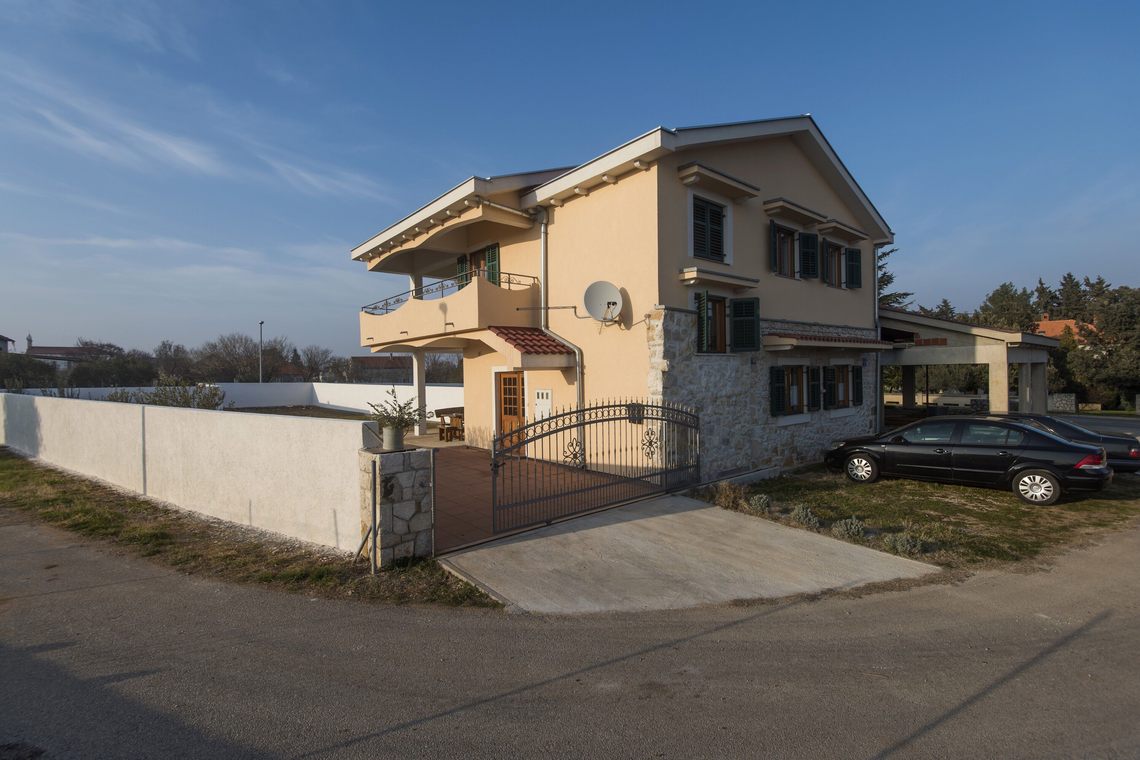 Une maison à deux étages avec un balcon, une antenne parabolique et une voiture garée dans l’allée.
