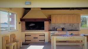 Uma cozinha com churrasqueira embutida, armários de madeira, uma mesa de jantar e uma janela com vista para o exterior.