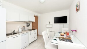 A modern kitchen with white cabinets, a dishwasher, and a dining area with a glass table and white chairs. - San Pedro Two bedroom apartment with sea view balcony (A2) (Sv. Petar na Moru)