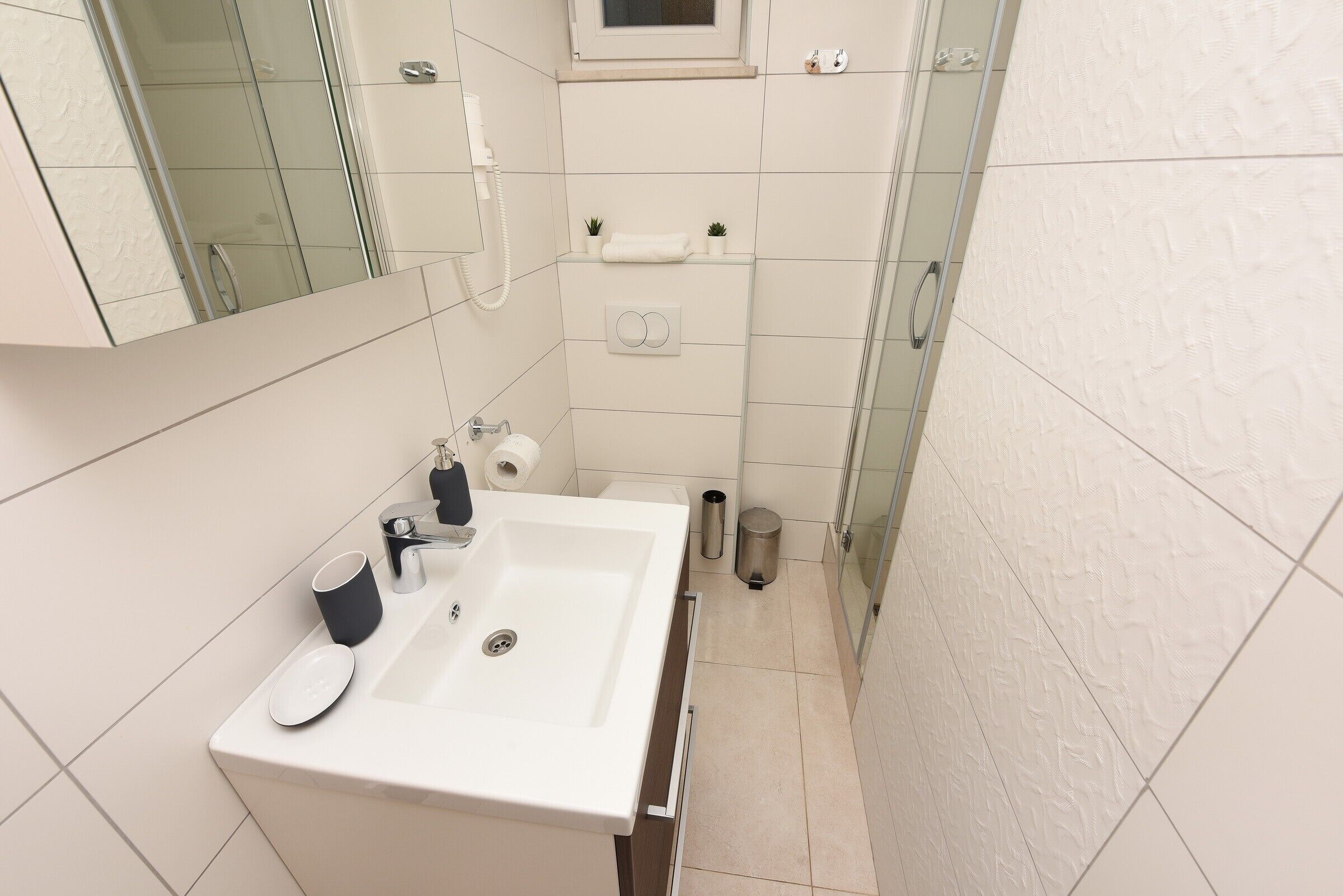 Un bagno moderno con un lavandino bianco, uno specchio e una cabina doccia in vetro.
