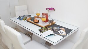 A modern dining area with a glass table, white chairs, a tray with a cookie, a glass of orange juice, a coffee cup, and a magazine. - San Pedro Two bedroom apartment with sea view balcony (A2) (Sv. Petar na Moru)