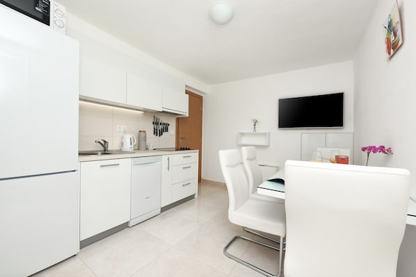 A modern kitchen with white cabinetry, a built-in oven, and a dining area with a white table and chair.