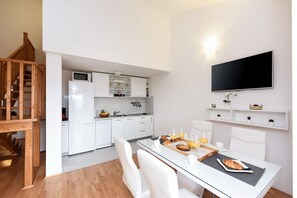 A modern kitchen with white cabinets, a microwave, and a flat-screen TV mounted on the wall.