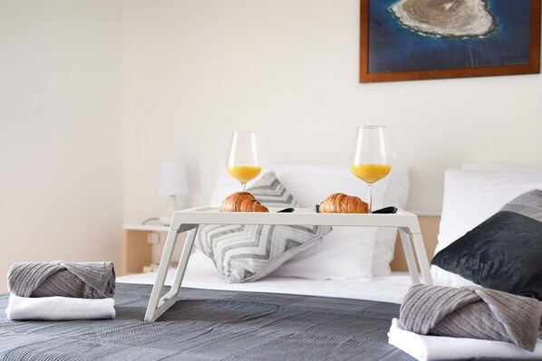 A neatly made bed with a white tray holding croissants and orange juice glasses, a pillow, and a rolled towel on the side.