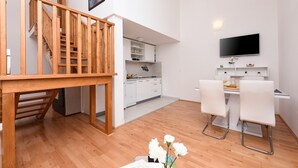 A modern kitchen with white cabinets, a wooden staircase, and a dining area with two white chairs.