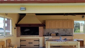 Een buitenkeuken met een bakstenen open haard, houten kasten en een eettafel.