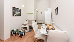 Een moderne, goed verlichte kamer met een eethoek, een bank en een klein tafeltje met drankjes.