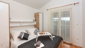 Een keurig opgemaakt slaapkamer met een bed, nachtkastje en een raam met dunne gordijnen.