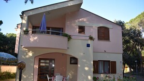 Un bâtiment à deux étages doté d’un balcon, d’un espace extérieur couvert aménagé en coin salon et d’un jardin fleuri.