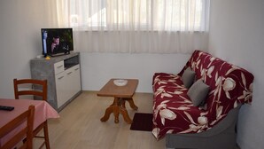 Un espace de vie compact comprenant un canapé, une petite table, un téléviseur posé sur un meuble et un coin repas avec une table et des chaises.