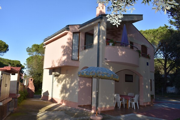 Une maison à deux étages avec un balcon, un coin repas comprenant une table et des chaises, et un parasol bleu.