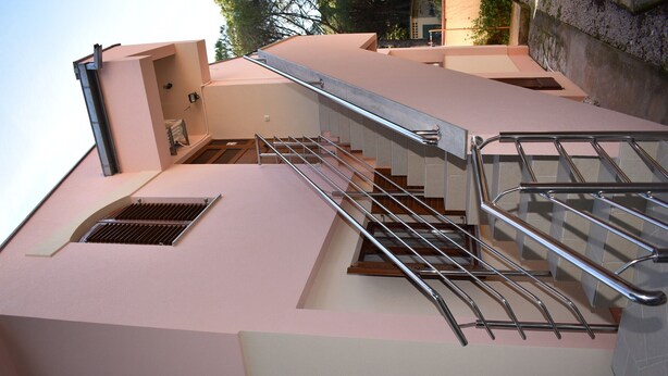 Un edificio moderno con fachada rosa, una escalera metálica con barandillas y un ventanal pequeño.