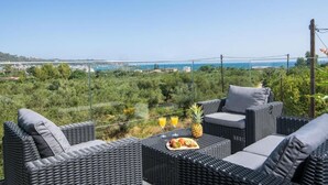 Un área de estar al aire libre con mimbre, con una mesa dispuesta con fruta y bebidas, con vistas a un paisaje costero.