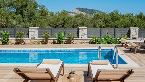 Una piscina con sillones de descanso y una pared de piedra con plantas.