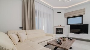 Una sala de estar moderna con un sofá color beige, una mesa de centro de madera, una chimenea y un televisor de pantalla plana montado en la pared.