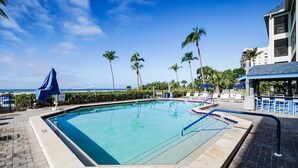 A swimming pool with a 3 ft depth marker, surrounded by palm trees and lounge chairs, with a view of the ocean in the background. - Now Open, Fully remodelled and restored (Fort Myers Beach)