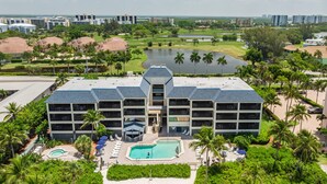 A hotel with multiple floors, a central pool, and a surrounding landscaped area with palm trees and a beach. - Now Open, Fully remodelled and restored (Fort Myers Beach)
