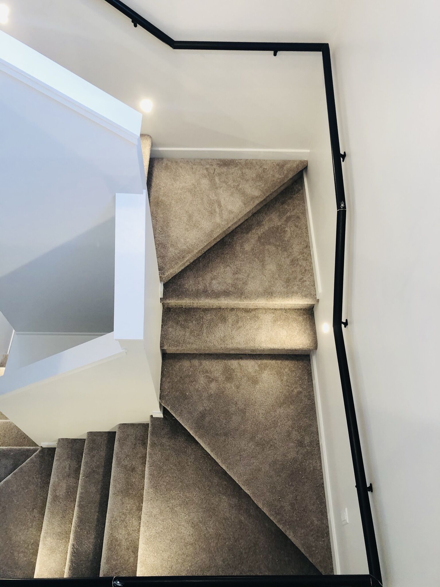 A modern staircase with a beige carpet and black handrails, leading to a white landing area.