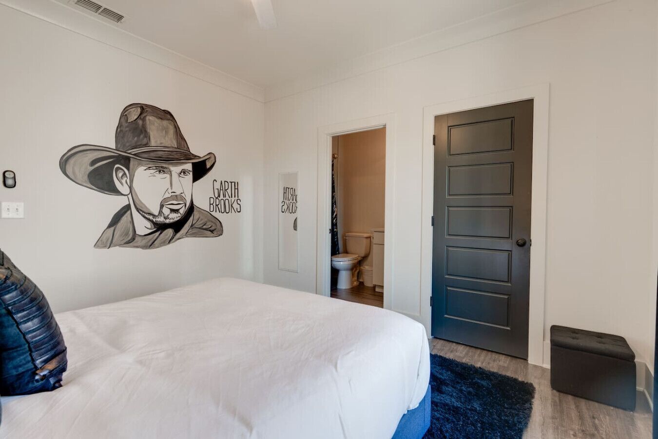 Une chambre à coucher avec un lit, une peinture murale, une porte et un petit tabouret.