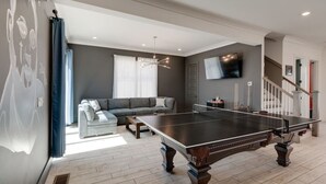 Ein Wohnzimmer mit Tischtennisplatte, einem grauen Sofa und einer Treppe.