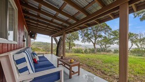 A covered outdoor seating area with a wooden table and a cushioned bench. - Hillside Paradise near Hidden Falls! Clean 3/1.5, Expansive views (Marble Falls)