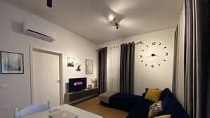 Una sala moderna con un televisor blanco, un reloj y un sofá con cojines.