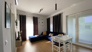 Una sala moderna con sofá, mesa de comedor y un ventanal con persianas.