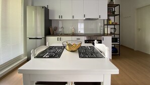 Una cocina moderna con armarios blancos, un refrigerador de acero inoxidable, un microondas y una mesa de comedor con posavasos negros.