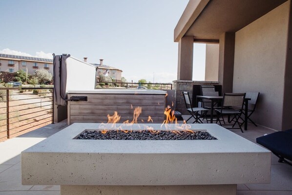 A rooftop patio with a concrete fire pit, outdoor furniture, and a view of a building with solar panels. - Suite With A View | Private Hot Tub (Washington)