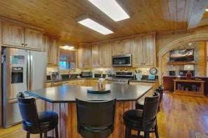 Une cuisine spacieuse avec des meubles en bois, un îlot central doté de tabourets et des appareils électroménagers modernes.