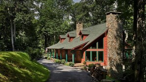 A lodge with a stone chimney, red exterior, and a paved driveway leading to the entrance.