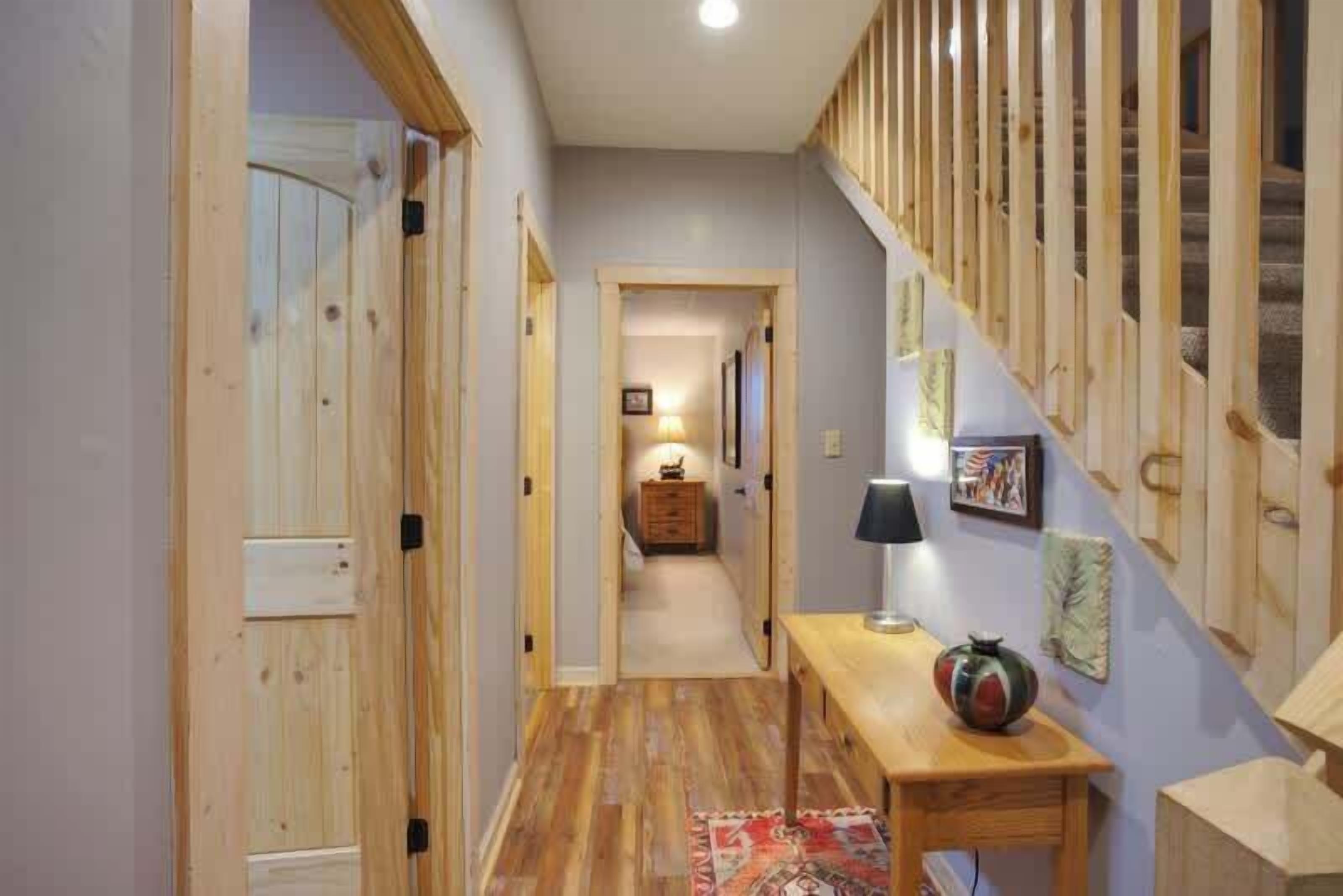 A wooden hallway with a wooden door, a table with a lamp, and a colorful rug.