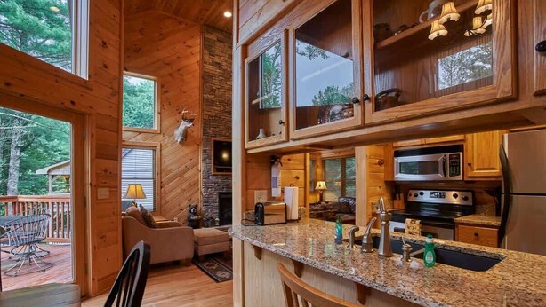 Ein Holzblockhaus-Interieur mit Küche, Essbereich und Kamin aus Stein.