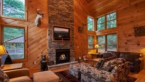 Ein gemütliches Blockhaus-Interieur mit Kamin aus Stein, Holzwänden, einem aufgehängten Hirschgeweih und einem Fernseher.