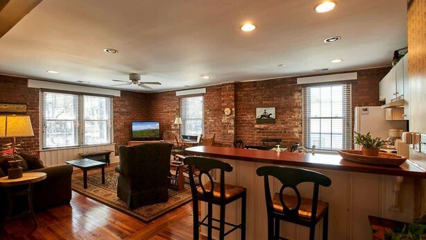 Un salon chaleureux avec un coin bar, des murs en briques et de grandes fenêtres.