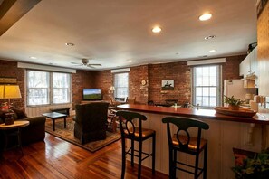 Un salon chaleureux avec un coin bar, des murs en briques et de grandes fenêtres.