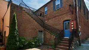 Un bâtiment en briques avec une porte bleue, un escalier et un petit jardin fleuri.