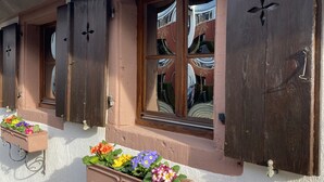 A building with wooden shutters, flower boxes with colorful flowers, and a tiled roof. - My mini house | 2 rooms | Smart TV | Stone & wood (Karlsruhe)