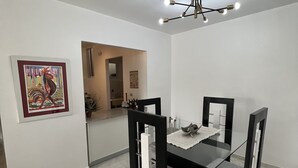 Una zona de menjador amb taula de vidre, cadires negres, lluminària al sostre i una obra d'art emmarcada a la paret.