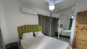 Un dormitori amb un llit, una tauleta de nit, un aparell d'aire condicionat, un ventilador de sostre i una porta corredissa de vidre.