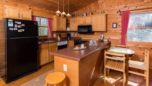 Eine Holzhütte mit einer Küche, die einen schwarzen Kühlschrank, Holzschränke, eine Mikrowelle und einen Esstisch mit Stühlen aus Holz beinhaltet.