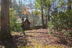 Ein rustikales Holzhäuschen, umgeben von einem Wald mit Holzzaun und herbstlichem Laub auf dem Boden.